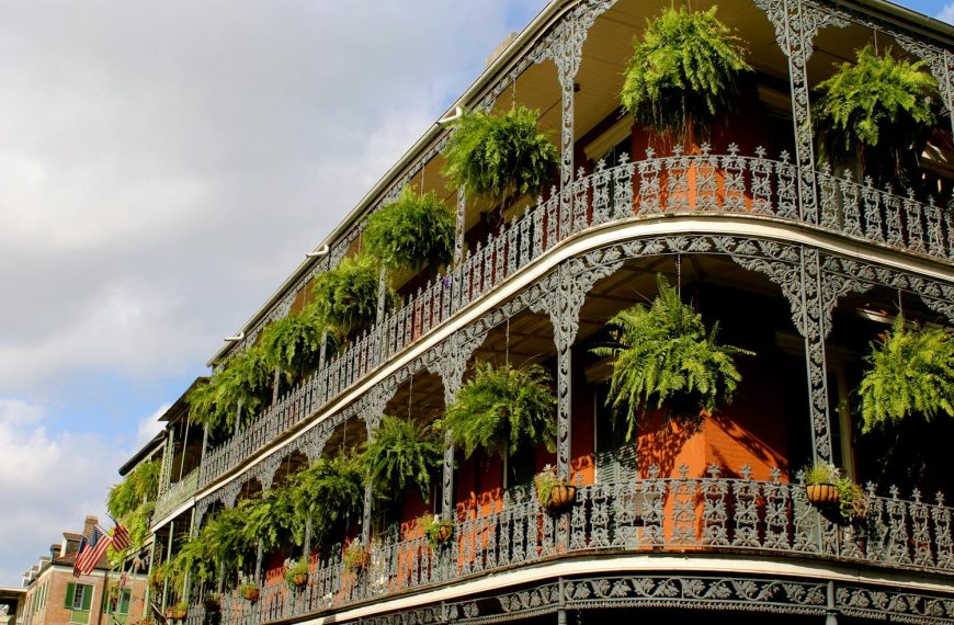 Detailed view of ornate ironwork balconies with lush greenery in New Orleans under a vibrant sky.